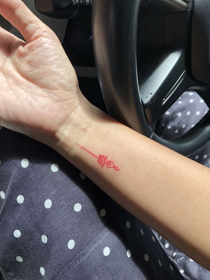 a woman's arm with a red ink tattoo on her left hand and a steering wheel