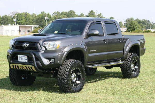 a gray toyota truck parked on top of a grass covered field with trees in the background