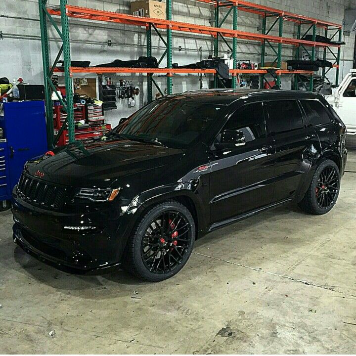 a black jeep parked in a garage next to other vehicles and tools on the shelves