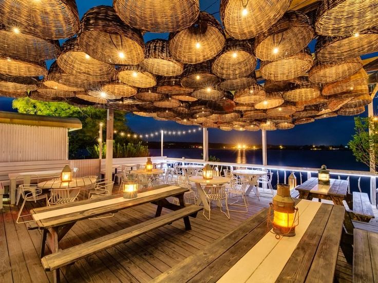 an outdoor dining area with lights and wicker baskets hanging from the ceiling above it