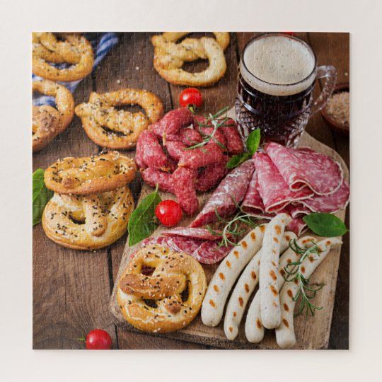 a wooden cutting board topped with assorted pretzels and meats next to a glass of beer