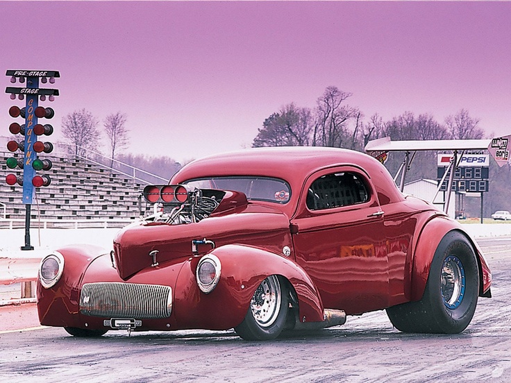 an old red car is parked on the side of the road in front of a stadium