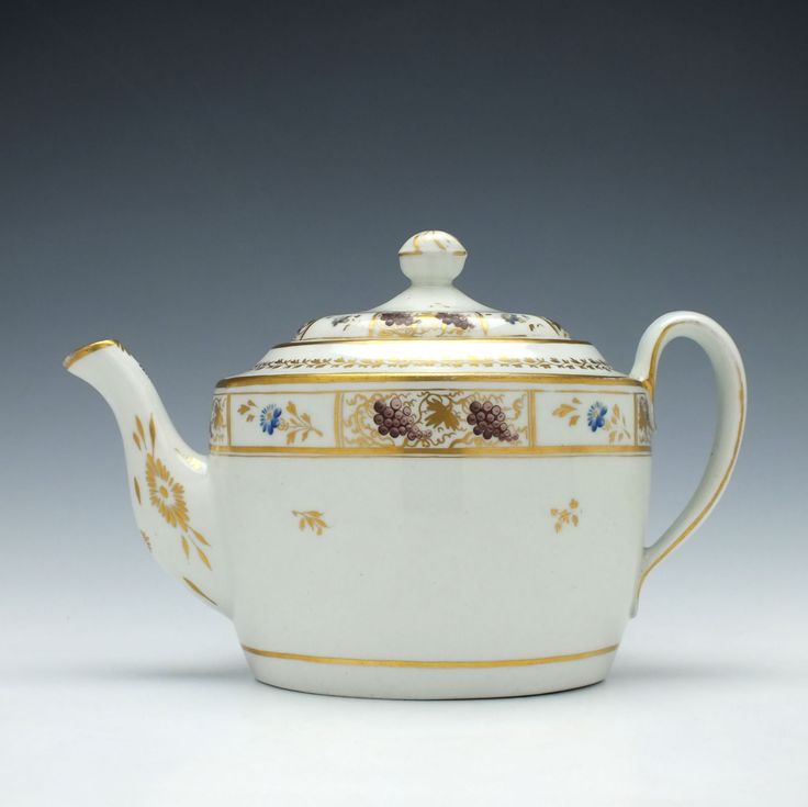 a white tea pot with gold trimmings and flowers on the top, sitting in front of a gray background