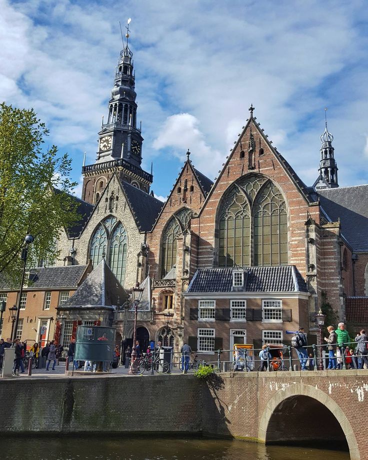 people are standing on the side of a bridge in front of an old church