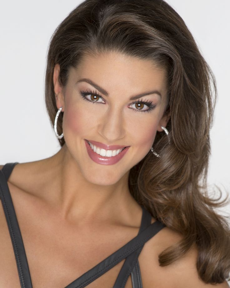 a woman with long brown hair and big hoop earrings on her head smiling at the camera