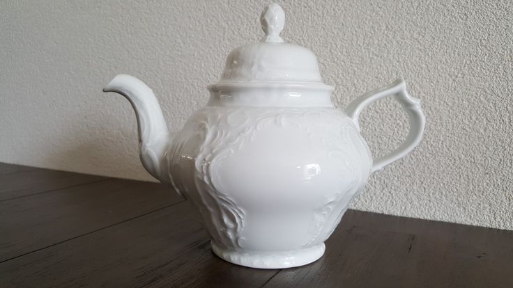 a white porcelain tea pot sitting on top of a wooden table next to a wall