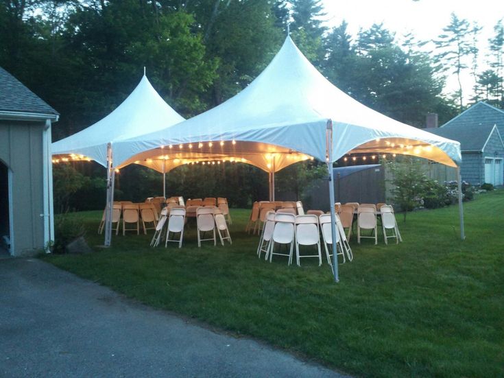 several tables and chairs are set up under white tents in the grass with lights on them