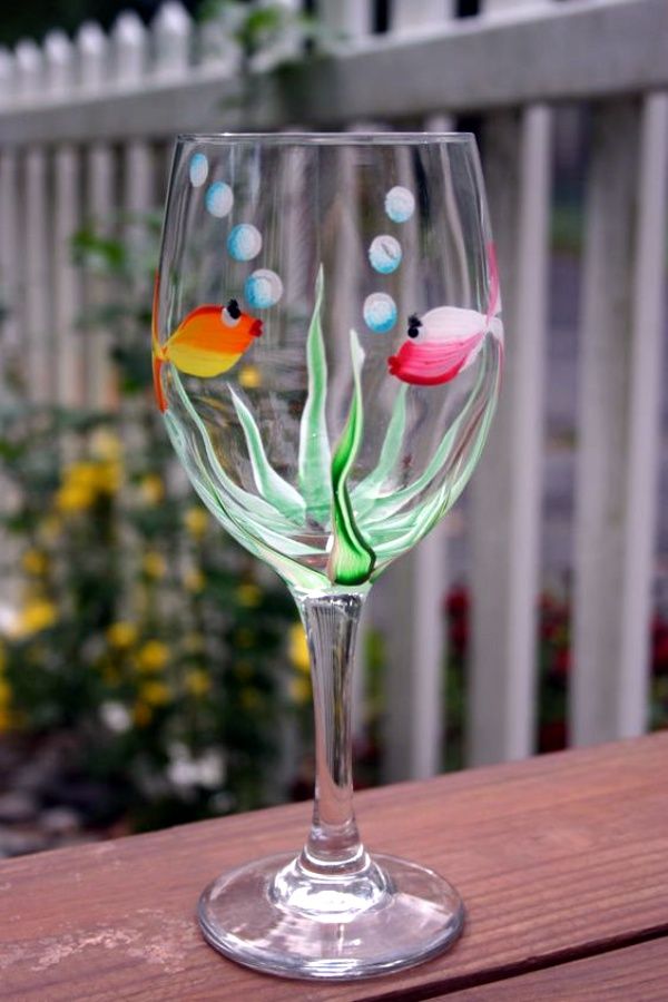 a wine glass with fish and bubbles painted on the bottom is sitting on a wooden table