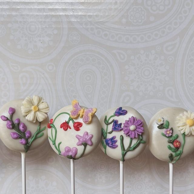 four cake pops decorated with flowers and butterflies