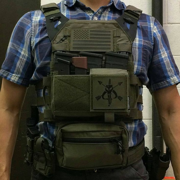 a man in plaid shirt standing next to a wall with an army vest on it