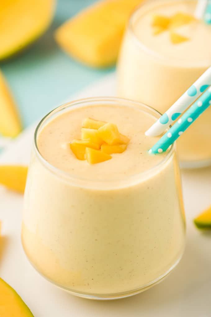 two glasses filled with smoothie next to sliced mangoes and slices of melon