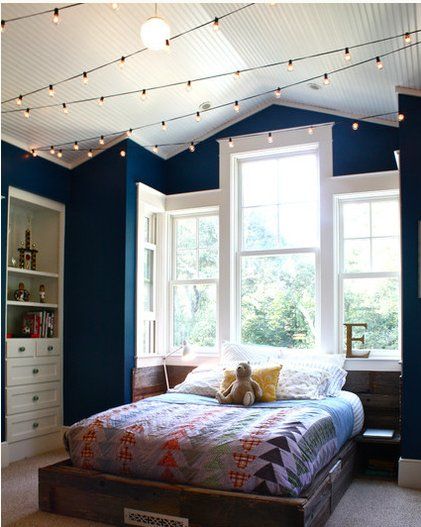 a bedroom with blue walls and lights strung from the ceiling