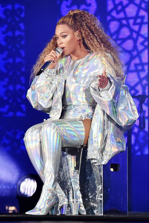 a woman in silver outfit on stage holding a microphone and wearing high heeled boots