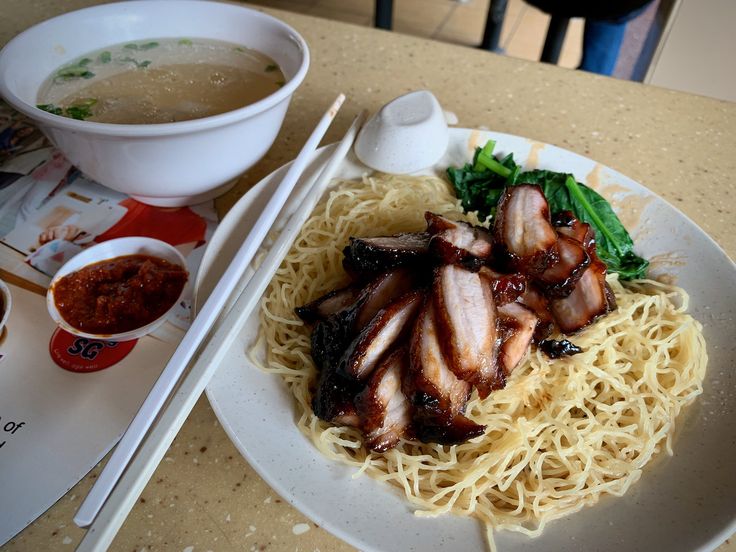 a white plate topped with meat and noodles next to a bowl of broccoli