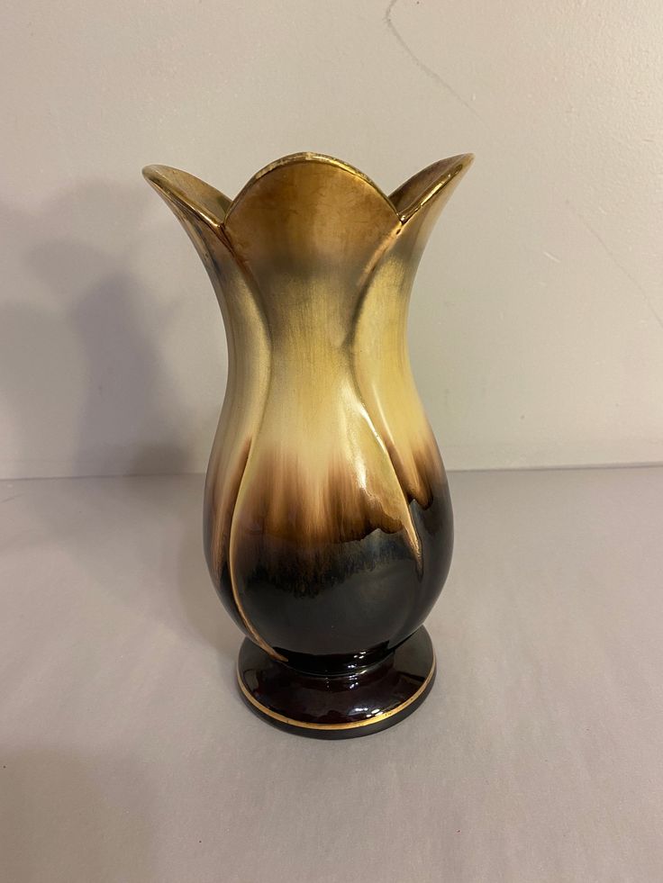 a black and gold vase sitting on top of a white table next to a wall