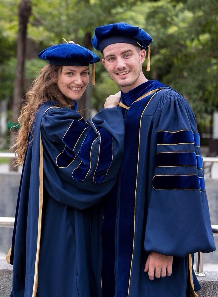 two people in graduation gowns posing for the camera