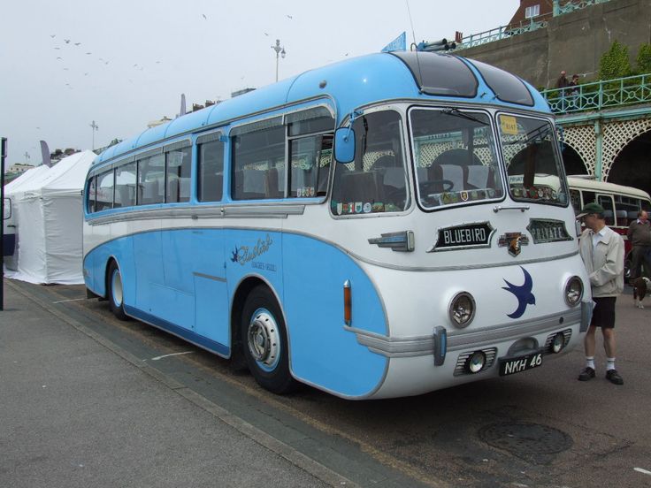 a blue and white bus is parked on the side of the road with people standing around it