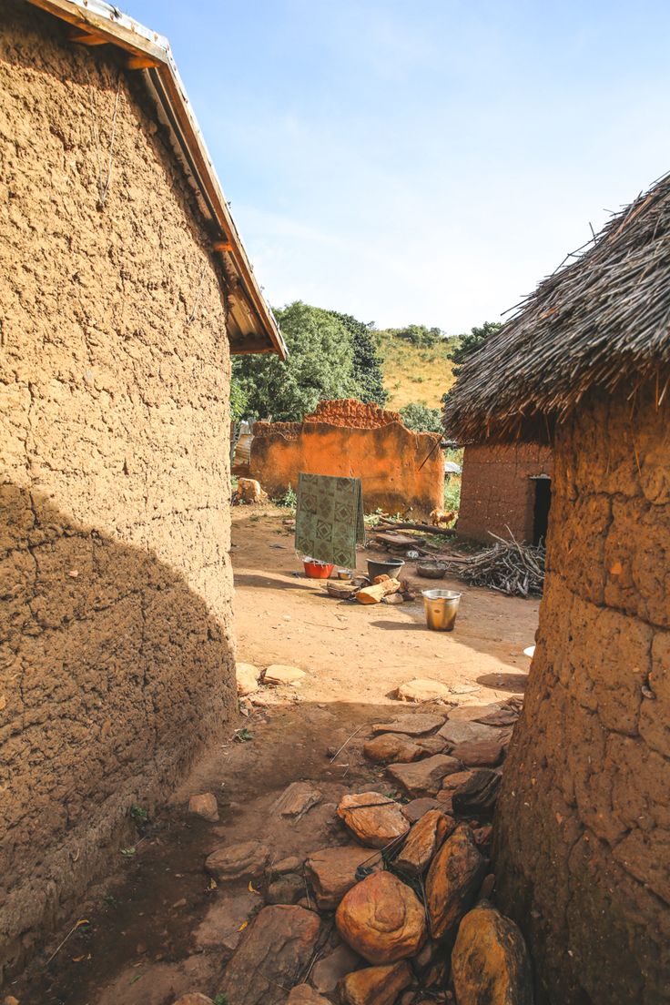 an old village with stone walls and grass roofing on the side of it, surrounded by rocks