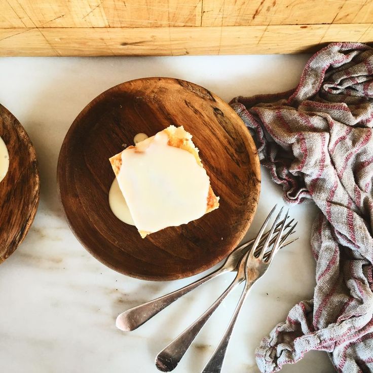 two wooden bowls filled with food on top of a white marble counter next to utensils