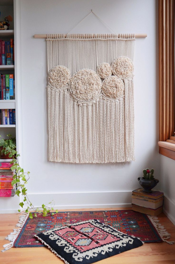 a white wall hanging with flowers on it next to a rug and bookshelf