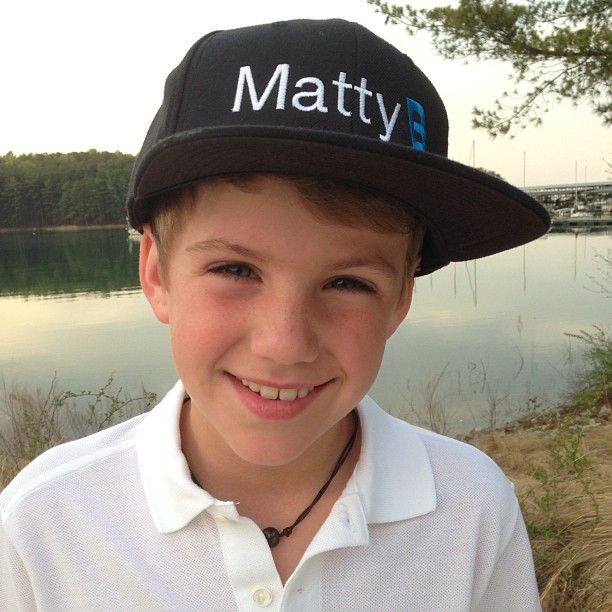 a young boy wearing a hat with the word mattty on it, standing in front of a body of water