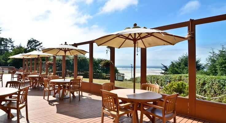 an outdoor dining area with tables and umbrellas on the deck overlooking the ocean in the distance