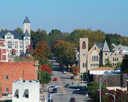 a city street lined with tall buildings and lots of trees in the fall time,