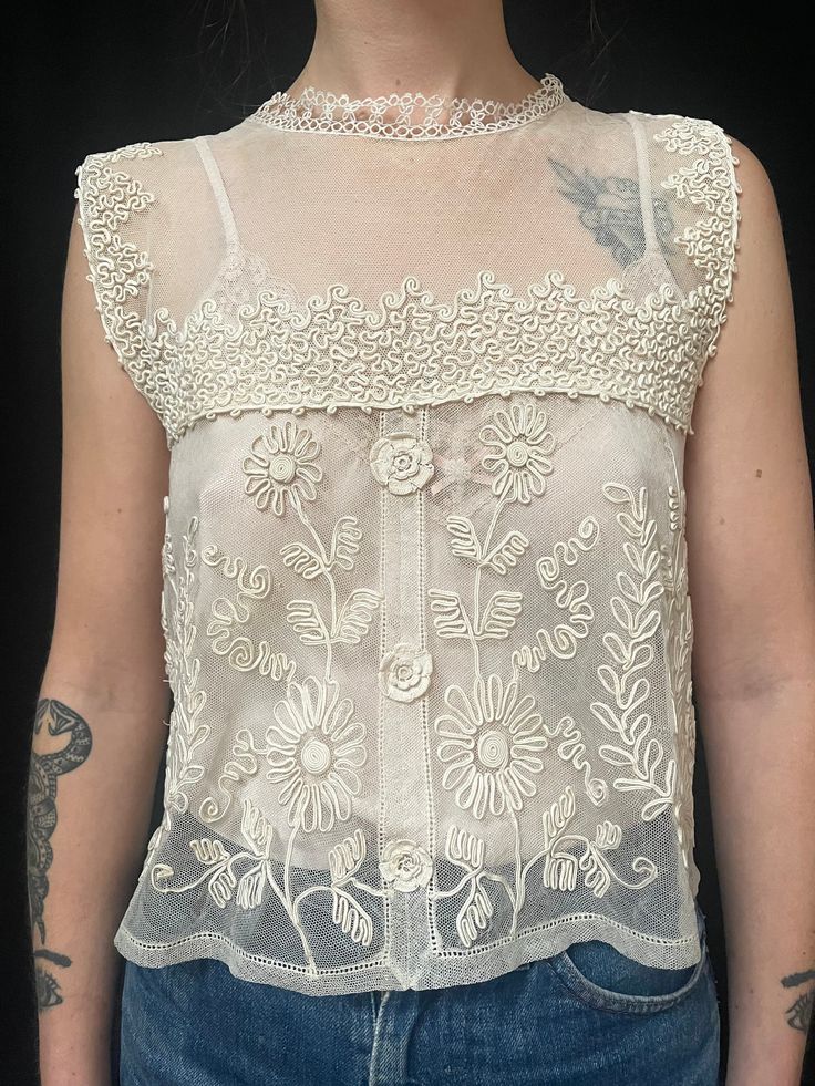 Item Details. From France C1930s this pretty and romantic lace camisole top which is covered in patterned of applied silk braid which has been stitched in decorative patterns (soutache) This lovely too would look great with jeans as shown in our photos or with a skirt or smart trousers for a more dressy look. The blouse fastens down the centre back with tiny hidden poppers. Measurements: All taken whilst garment is laying flat. Our model Amie is a UK size 8. Across front 43cm (17 inches) Length from shoulder to hem 49cm (19.5 inches) Condition. In excellent wearable condition.  All of our specially chosen pieces are antique and have the idiosyncrasies of antique and loved garment so small marks, stains and signs of wear are to be expected and are an inherent part of their charm and history Fitted Lace Crochet Camisole Top, Victorian Fitted Tops For Summer, Fitted Victorian Summer Tops, Fitted Victorian Tops For Summer, Vintage Camisole Top For Daywear, Fitted Camisole With Crochet Lace, Vintage Lace Patchwork Tops For Summer, Spring Vintage Crochet Top With Lace Work, Vintage Lace Top Sleeveless Camisole