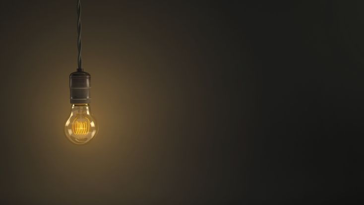 an illuminated light bulb hanging from a wire on a dark background with only one lightbulb visible