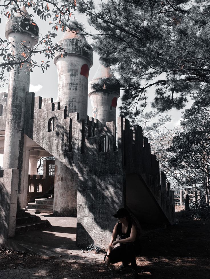 a man sitting on the ground in front of a castle like structure with two towers