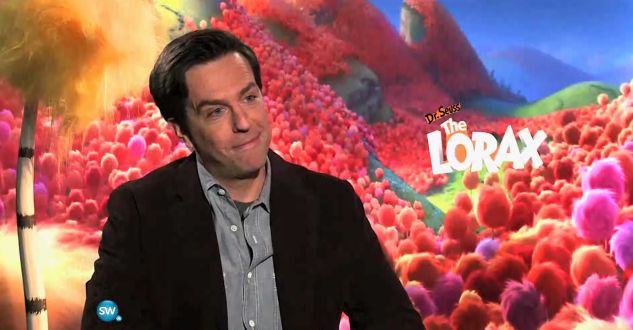 a man sitting in front of a colorful wall with the lorax logo on it