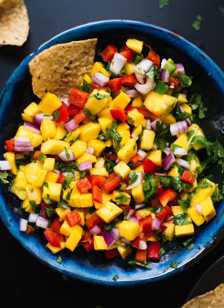 a blue bowl filled with fruit and veggies next to tortilla chips