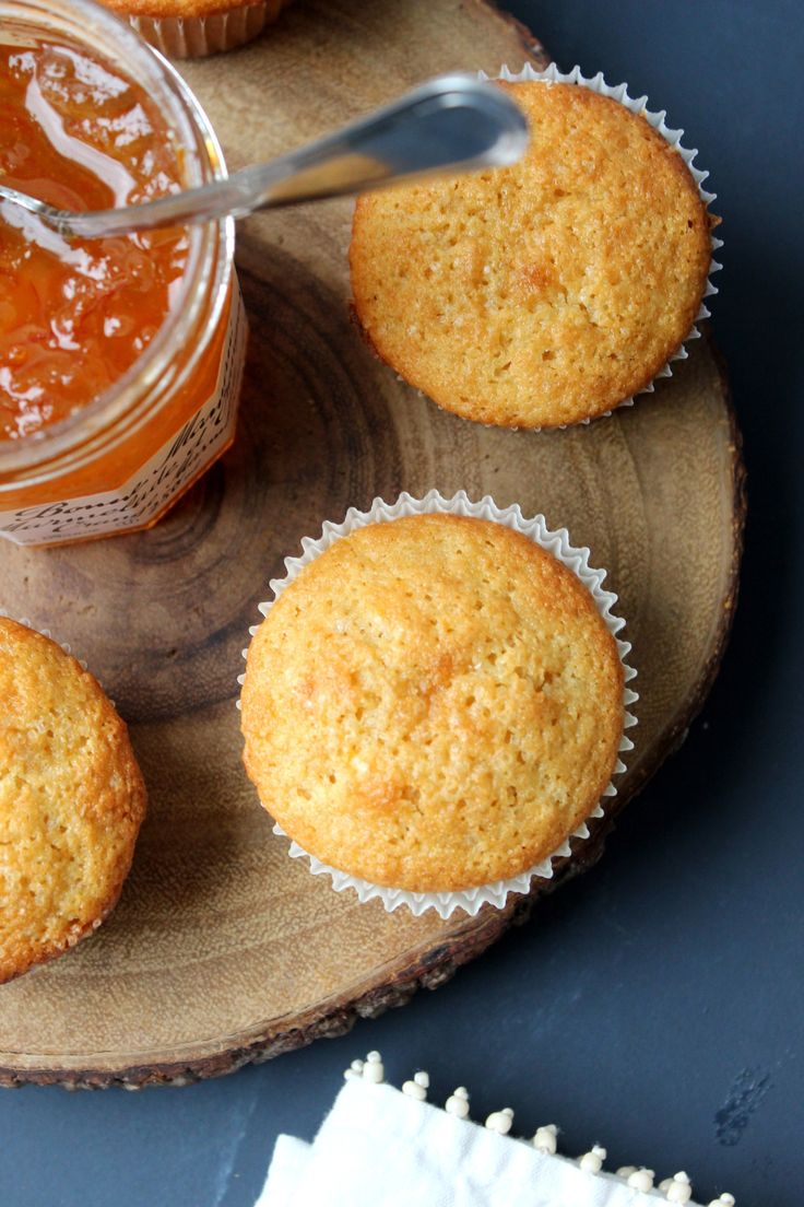 three muffins sitting on a wooden plate next to a jar of jam