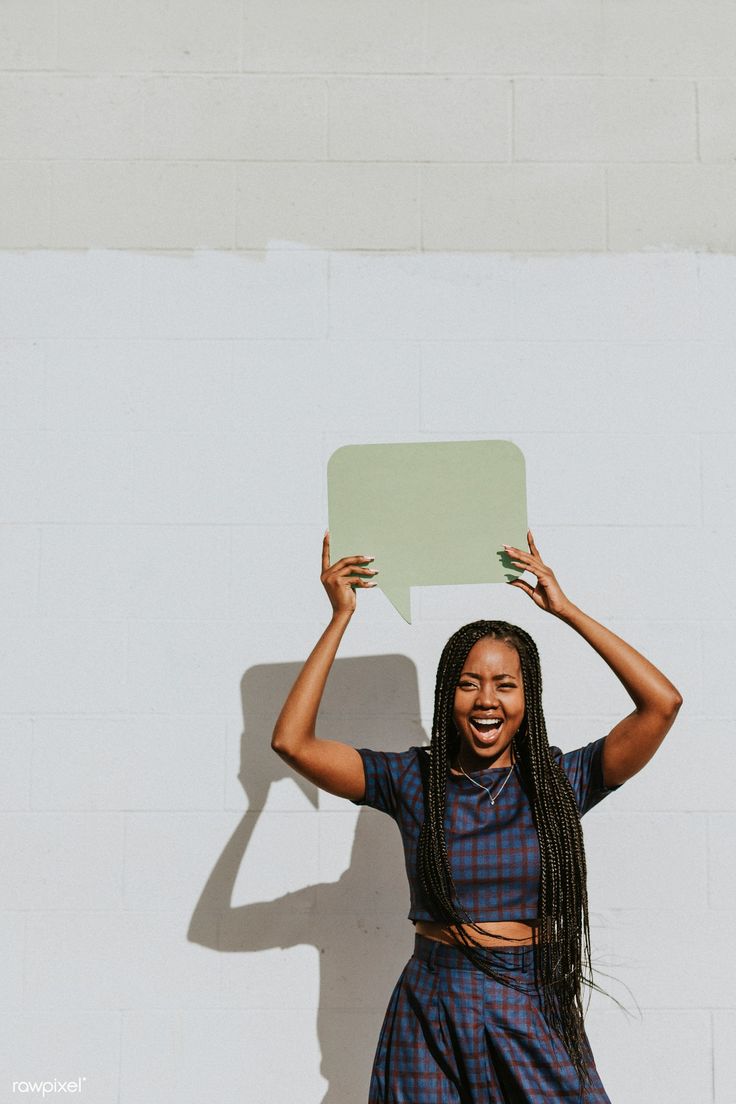 a woman standing in front of a white wall holding up a speech bubble