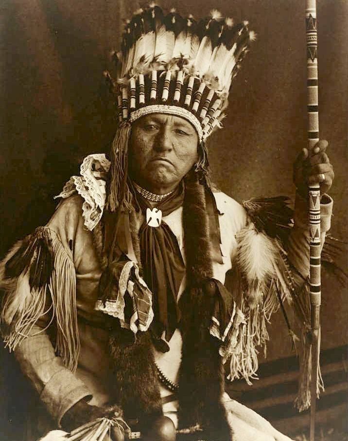 an old black and white photo of a native american man with feathers on his head