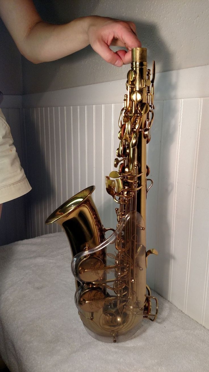 a gold colored saxophone sitting on top of a white sheet covered table next to a person's hand