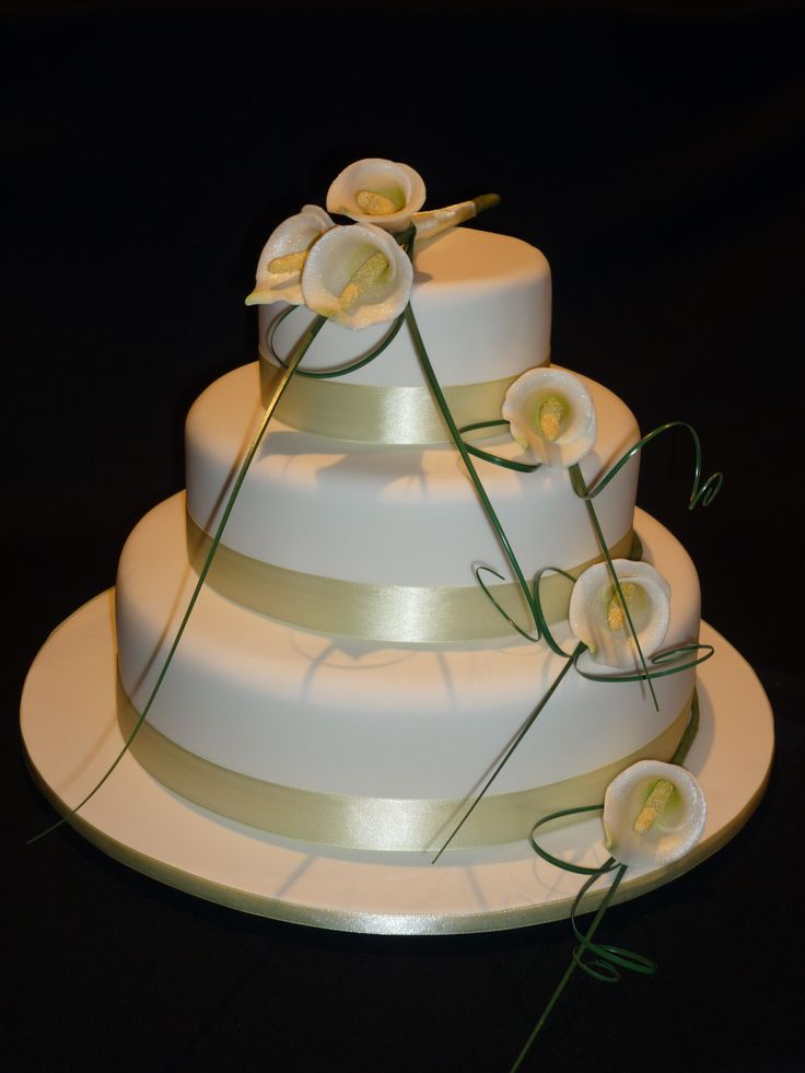 a three tiered cake with white flowers on top and green stems sticking out of it