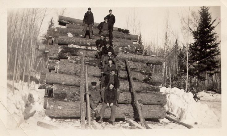 black and white photograph of men standing on logs in the snow