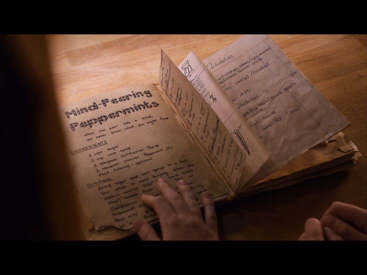 an open book with writing on it sitting on top of a wooden table next to someone's hand