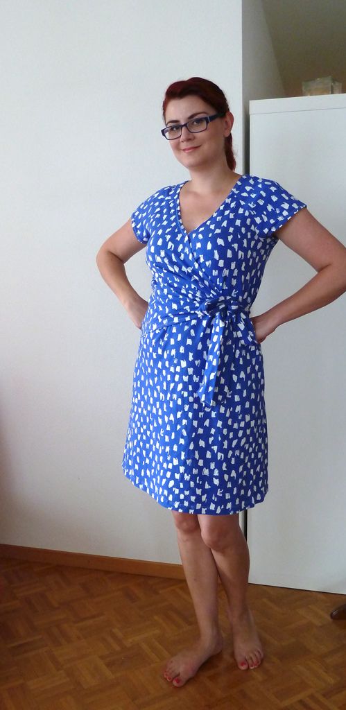 a woman standing in front of a wall wearing glasses and a blue dress with white polka dots