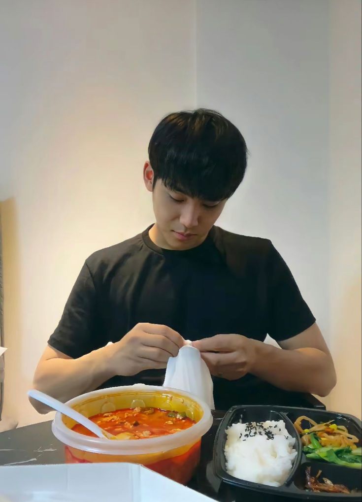 a man sitting at a table with food in front of him and looking down on his phone