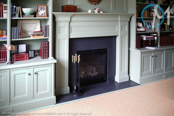 a living room with a fire place and bookshelves on the wall above it