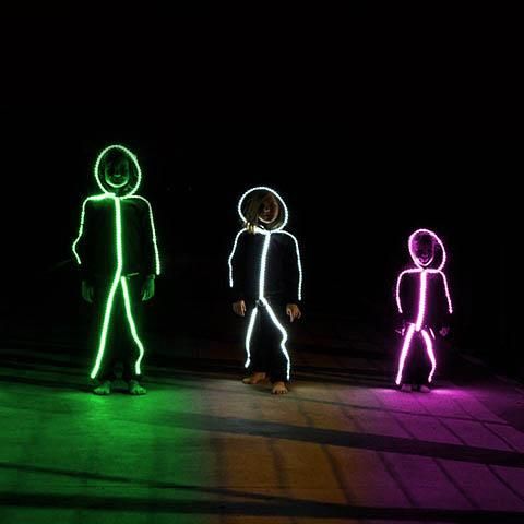 three people standing in the dark with neon lights on their faces and hands, all looking different directions