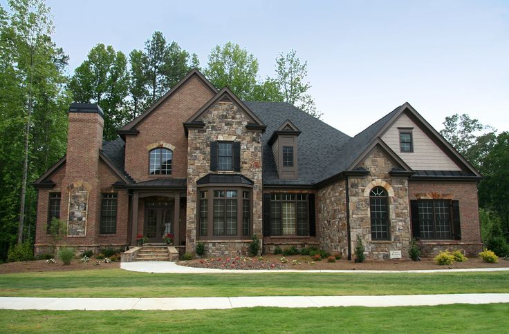 a brick and stone house in the middle of a grassy area with trees behind it