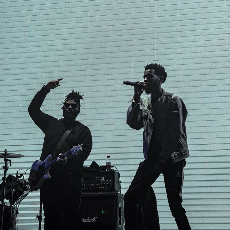 two men standing next to each other on stage with microphones in their hands and one man holding a guitar