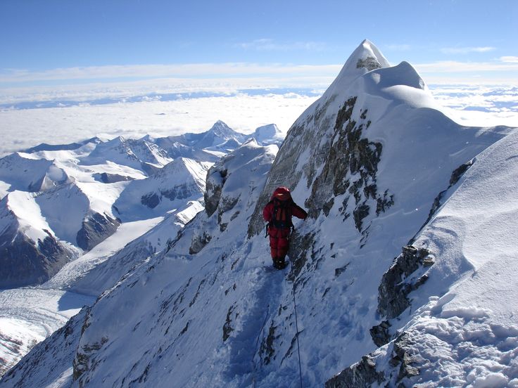 a man climbing up the side of a snow covered mountain with mountains in the background