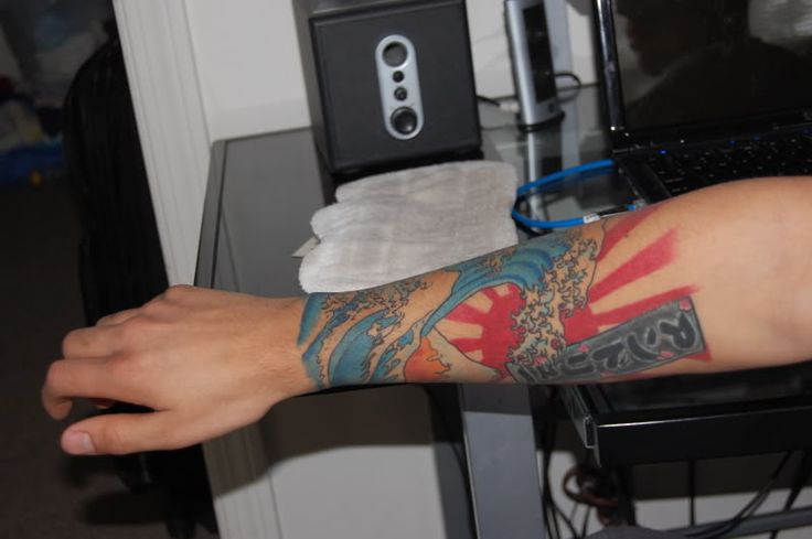 a man with tattoos on his arm sitting in front of a computer monitor and keyboard