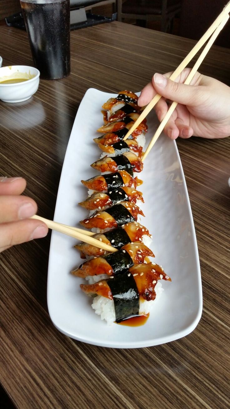 two hands holding chopsticks over a plate of sushi on a wooden table