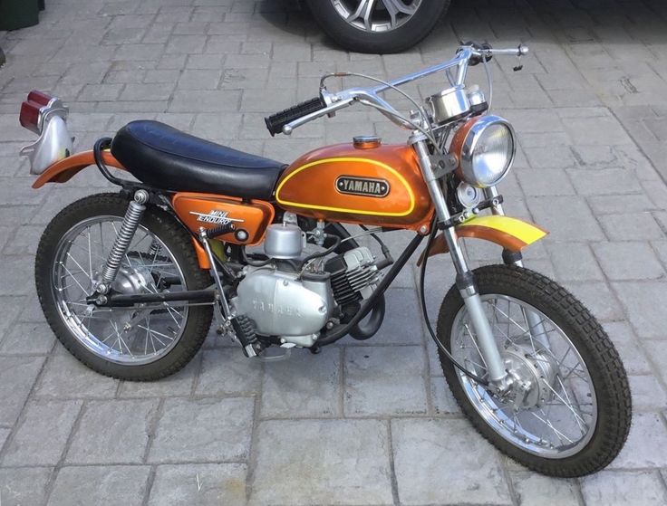 an orange and black motorcycle parked on the side of a brick road next to a car