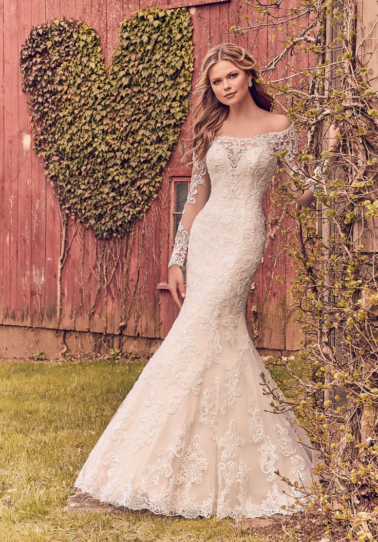 a woman standing in front of a red barn wearing a wedding dress with long sleeves